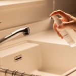 キッチンのシンクに向かって洗浄用スプレーを吹きかけている手のアップ画像。